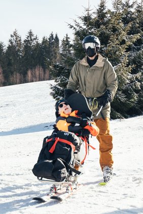 Portrait von einem Biskifahrer und seinem Begleitläufer. Der Begleitläufer trägt eine große, verspiegelte Skibrille.